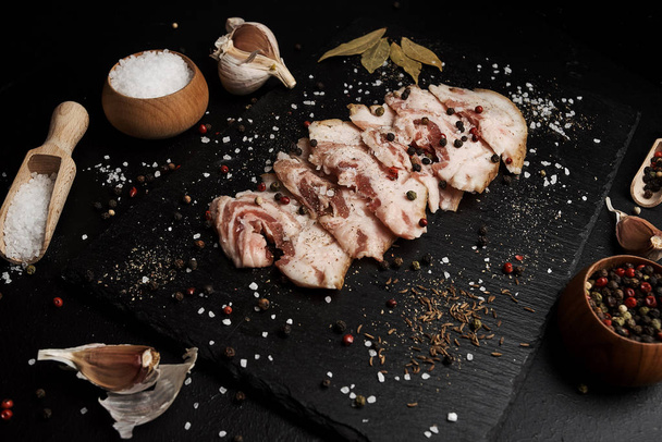 food composition with ham slices on cutting board surrounded by salt and pepper on table - Fotó, kép