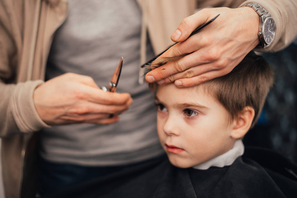 cropped image of barber making haircut of little boy at salon - 写真・画像