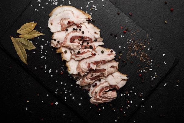food composition with ham slices on cutting board surrounded by salt and pepper on table - Фото, зображення