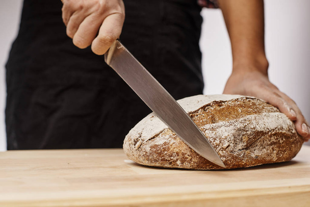 cropped shot of female baker cutting fresh baked bread  - Фото, зображення