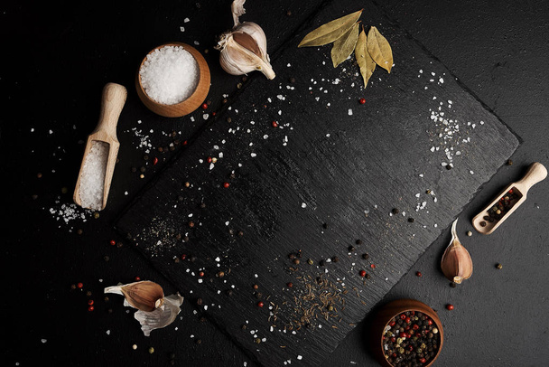food composition with garlic on cutting board surrounded by salt and pepper on table - Photo, Image