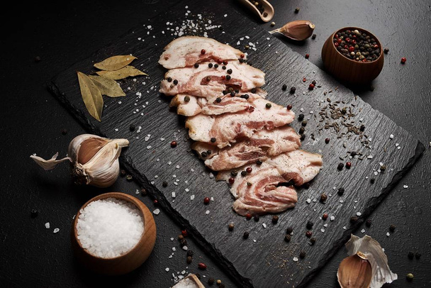 food composition with ham slices on cutting board surrounded by salt and pepper on table - Photo, Image