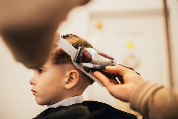 cropped image of barber making haircut of little boy at salon - Fotoğraf, Görsel