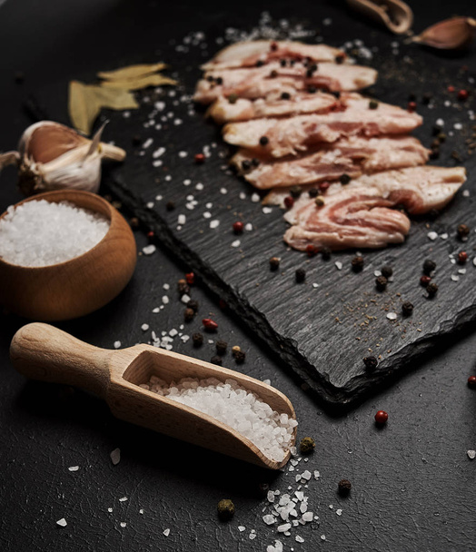 food composition with ham slices on cutting board surrounded by salt and pepper on table - Фото, зображення