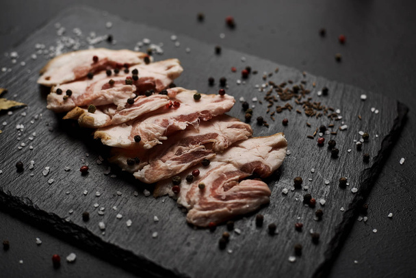 food composition with ham slices on cutting board surrounded by salt and pepper on table - Фото, изображение