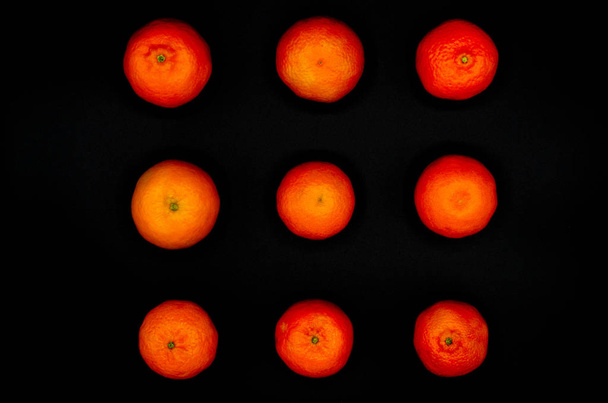 Свіжі помаранчеві мандарини утворюються симетрично і сильно контрастують на чорному тлі
 - Фото, зображення