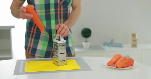 Man grates carrot on stainless steel grater - Imágenes, Vídeo