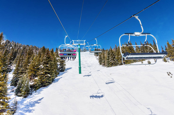 Esquiadores no identificables en telesilla subiendo una pista de esquí en la cordillera nevada de las Montañas Rocosas Canadienses
. - Foto, imagen