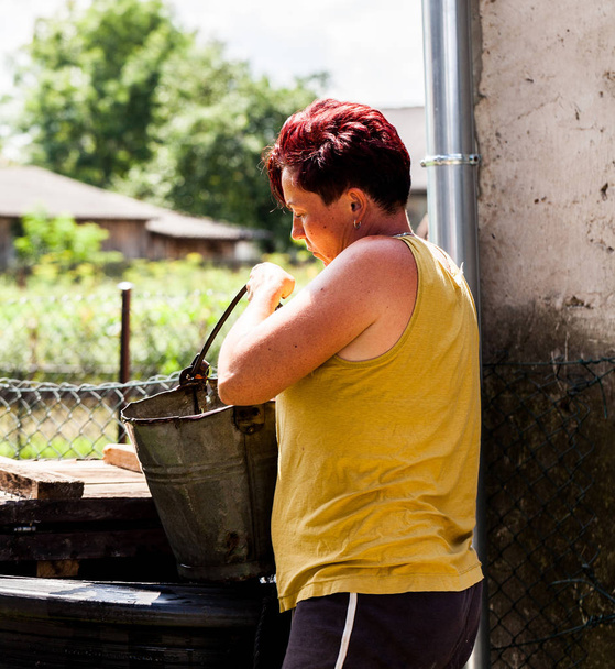Une vue d'une femme tenant un seau métallique regardant profondément. La femme récupère l'eau du puits naturel. Typique corvée de ménage. Scénario de zone rurale
. - Photo, image