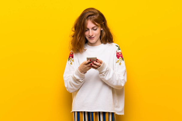 Jeune rousse femme sur le mur jaune envoyer un message avec le mobile
 - Photo, image