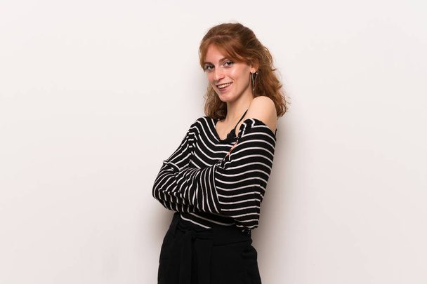 Young redhead woman over white wall keeping the arms crossed while smiling - Foto, imagen