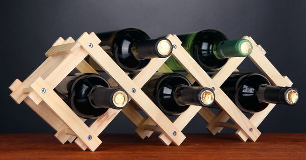 Bottles of wine placed on wooden stand on grey background - Foto, imagen