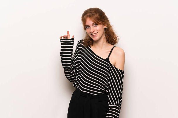 Young redhead woman over white wall saluting with hand with happy expression - Photo, image
