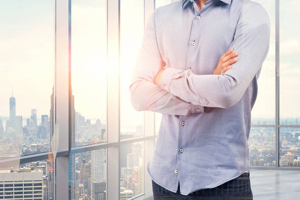 Неузнаваемый бизнесмен в синей рубашке, стоящий со скрещенными руками в панорамном офисе. Тонированное изображение
 - Фото, изображение