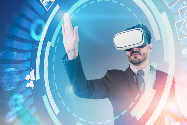 Serious young businessman with beard wearing suit and vr glasses working with hud internet interface. Toned image double exposure - Фото, зображення