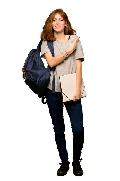 eine Ganzkörperaufnahme einer jungen rothaarigen Studentin, die zur Seite zeigt, um ein Produkt auf isoliertem weißem Hintergrund zu präsentieren - Foto, Bild