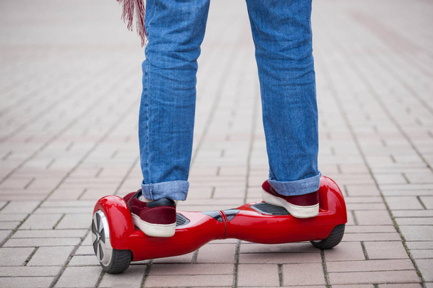 Feet of a girl riding on modern red electric mini segway or hover board scooter. Trending new transportation technology that is so much fun and easy to ride and produces no air pollution to the atmosphere. Close up on model legs and gadget. - Photo, Image
