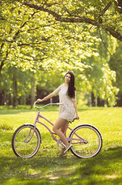 Young girl in sundress riding a bicycle in park - Fotó, kép