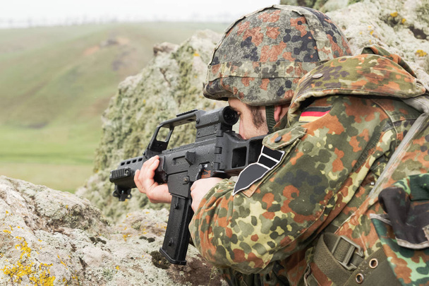 Young white soldier in bulletproof helmet shooting with automatic rifle outdoor.National guard protecting peace with firearms.Border patrol protects country with guns.Sniper shoots with optical scope - Fotoğraf, Görsel