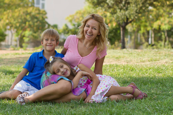 Beautiful young lady and her cute children posing in the green park at bright summer day - Foto, Imagen