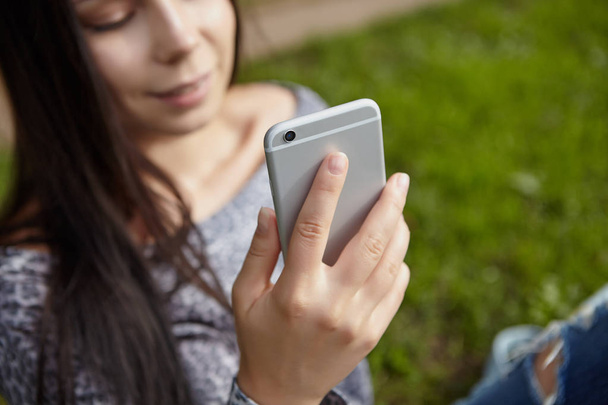 Trendy smartphone in hands of young brunette girl. Popular big silver phone model - Foto, imagen
