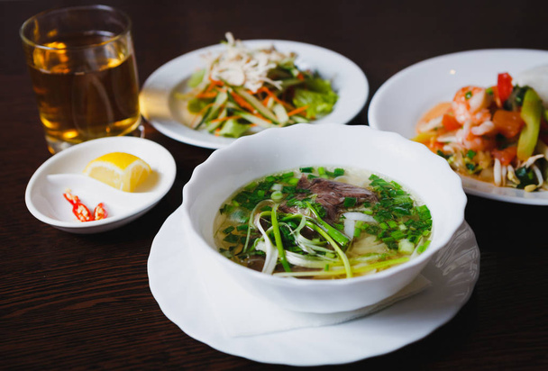 Deliciosa comida vietnamita para la cena en restaurante exótico.Disfrute de sabrosa sopa pho bo y ensalada con ingredientes vegetales naturales.Menú de almuerzo de negocios asiático en la mesa en la cafetería
 - Foto, Imagen