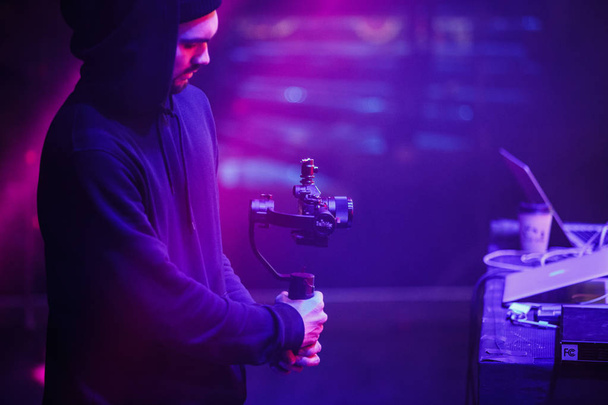 MOSCOW - 16 FEBRUARY,2017: Young video camera man film concert on stage with portable steady cam and small modern dslr camera in hand.Night club entertainment show filming - Fotoğraf, Görsel