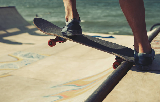 Teenager skater boy feet on skateboard deck in skatepark. Extreme sports background. Cool summer sport festival outdoor. Skateboarder rides on wooden mini ramp obstackle - Foto, afbeelding