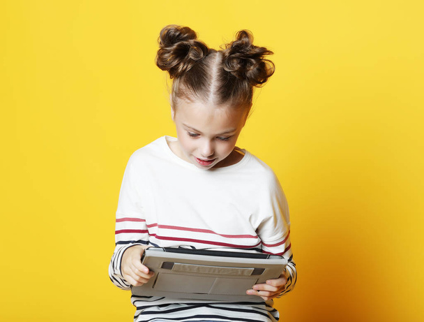 Little girl with tablet on yellow studio background. - Фото, зображення