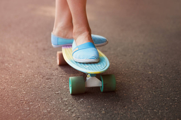 Feet of girl riding colorful short cruiser longboard. Modern trendy skateboard model. - Фото, изображение