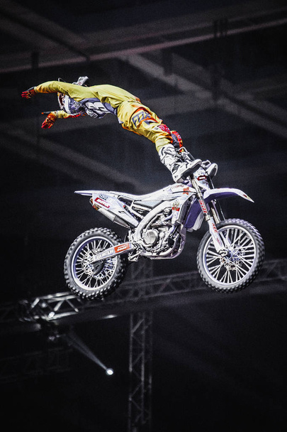 MOSCOW - 14 MARCH, 2015: Extreme sport competition show Proryv. Freestyle motocross athlete jumps high from big air ramp performing dangerous cliff hanger trick on FMX motor bike - Fotoğraf, Görsel