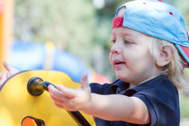 Portrait of cutest blond baby boy swinging on the playground - 写真・画像