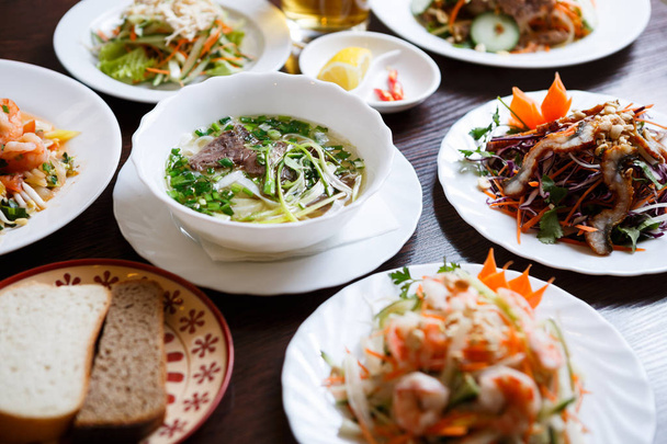 Exotic Vietnamese food restaurant menu close up.Traditional Asian dish served on white plate.Big dinner with pho bo soup,fresh vegetable diet salad - Fotografie, Obrázek