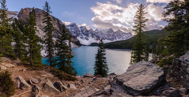 Moraine Lake in Banff National Park, Alberta, Canada at sunset with mountain peaks, forest, rocks, water and trees - Photo, Image