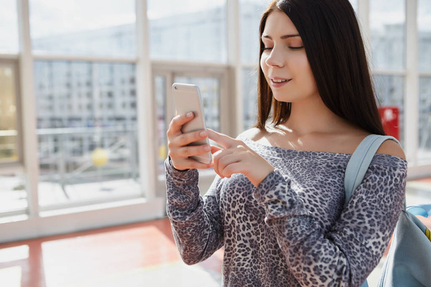 Happy young brunette girl using modern silver smart phone. Attractive female model, popular trendy phone model - Фото, изображение