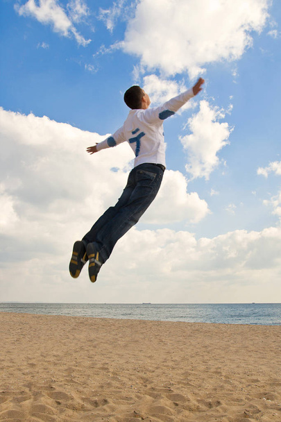 Guy jumping into the sky at the beach - Фото, изображение