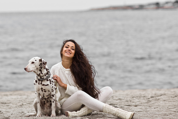 Onnellinen nuori nainen lepää rannalla syksyllä koiran kanssa
 - Valokuva, kuva