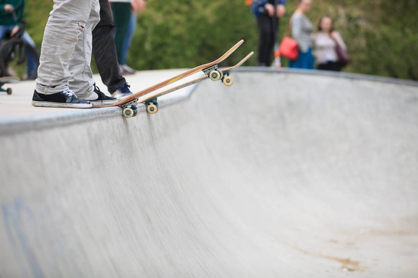 Skateboarder de pé em uma rampa no parque de skate pronto para andar de skate e fazer truques. Parque exterior de concreto, foco em skate, pés e sapatos
 - Foto, Imagem