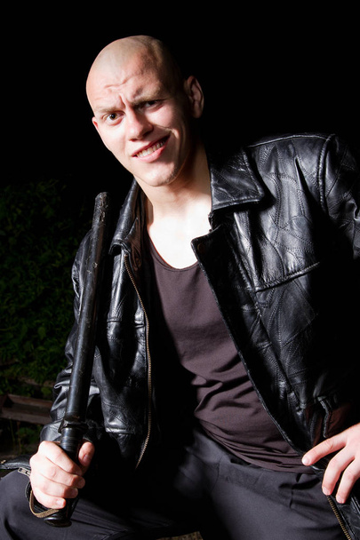 Bald athletic thug in black leather jacket and sportive costume armed with police baton - Zdjęcie, obraz