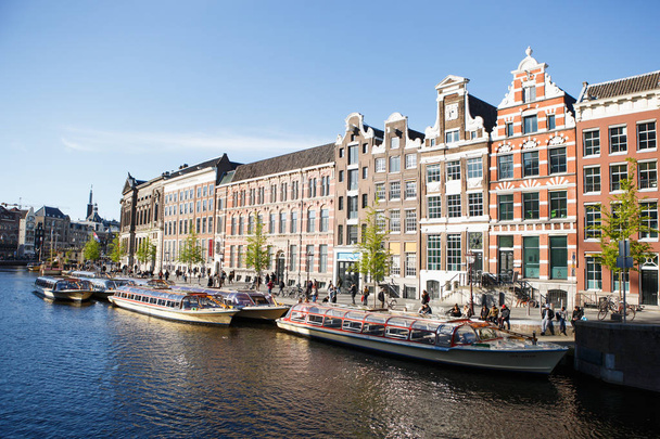 AMSTERDAM,NETHERLANDS-27 APRIL,2019: Flotaing houseboats in canal of river Amstel in historic center of Amsterdam city.Popular dutch boat houses drifting on water,moored on a pier - Φωτογραφία, εικόνα