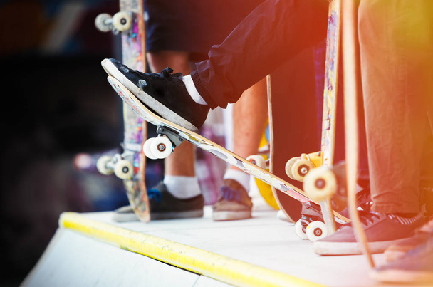 公園でスケート ボードに乗って若いスケーターの男の子のグループ。晴れた夏の日。青少年のための極端なスポーツ活動。10 代の人気のあるスポーツ。スケートボーダーの足とデッキに焦点を当てる - 写真・画像