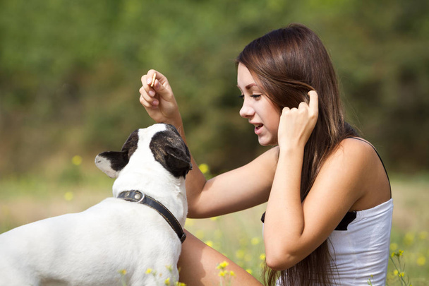 Teenage brunette girl playing with her healthy young bulldog in the park - Photo, Image