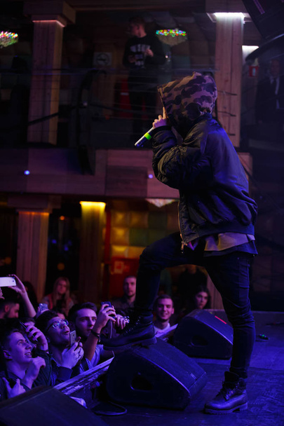 MOSCOW - 16 FEBRUARY, 2017: Young white Russian rap singer performs on stage in trendy camo hoodie coat. Rapper sings on scene in night club during music festival. Jazz Cartier hip hop party performer - Fotoğraf, Görsel
