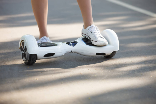 Feet of girl riding electric mini hover board scooter outdoors in park. Ecological city transportation on battery power, produces no air pollution to atmosphere - Photo, Image