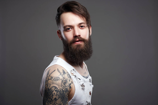 Um homem bonito com barba. Hipster barbudo. Menino com corte de cabelo elegante e tatuagem
 - Foto, Imagem
