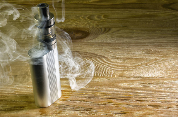 Електронна сигарета стоїть на столі в хмарі пари
 - Фото, зображення