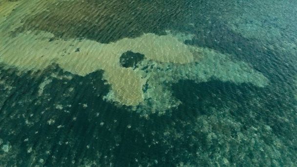 prachtige luchtfoto drone foto van een grote koraal rif voldoen aan een zandstrand in kalm weer plat water en ongelooflijk kleurrijke zee oceaan bed rond een kleine geïsoleerde afgelegen tropische eiland - Foto, afbeelding