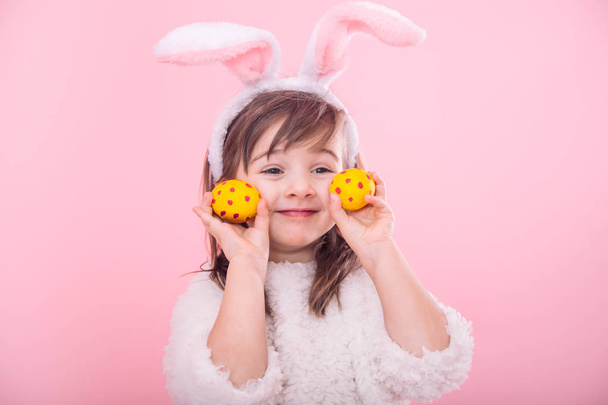 Portrait of a cute little girl with Bunny ears and yellow Easter eggs in red polka dots isolated on pink background - Photo, Image