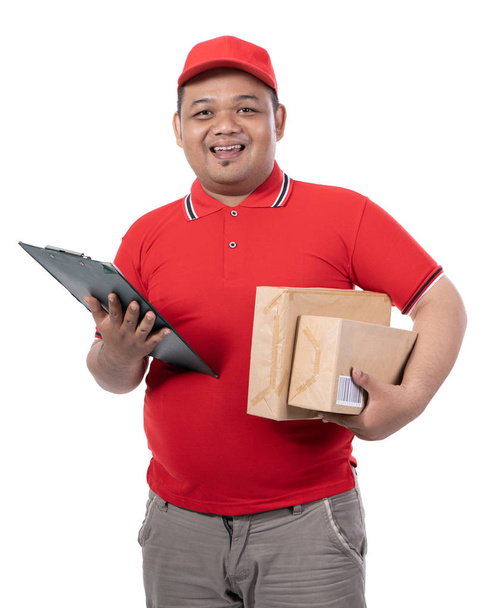 portrait of young man with red uniform delivering boxes and holding clipboards look at the camera - Фото, изображение