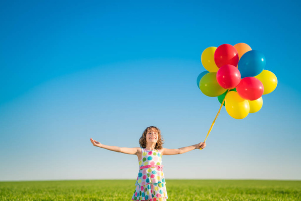Onnellinen lapsi leikkii kirkkaita monivärisiä ilmapalloja ulkona. Poika pitää hauskaa vihreällä kevätkentällä sinistä taivasta vasten. Terveellisen ja aktiivisen elämäntavan käsite - Valokuva, kuva